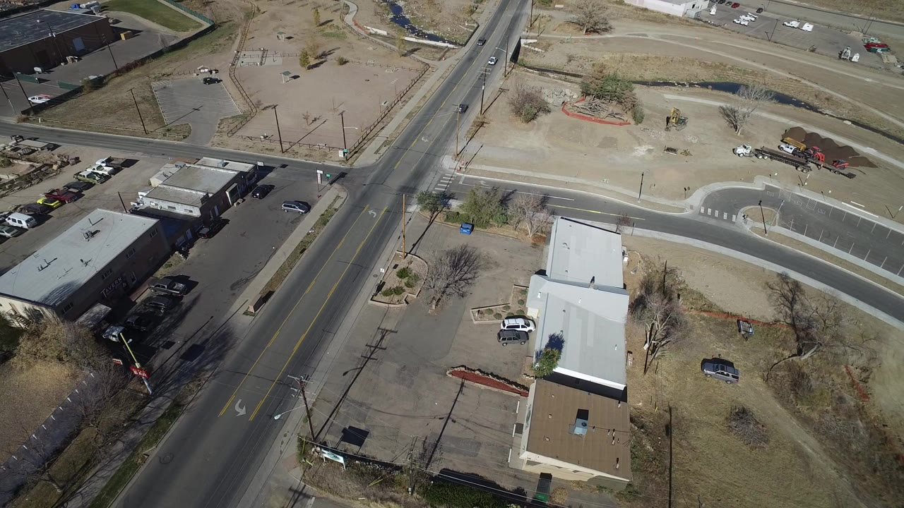 High aerial view of a road intersection, parking lots, low buildings, and scattered cars.
