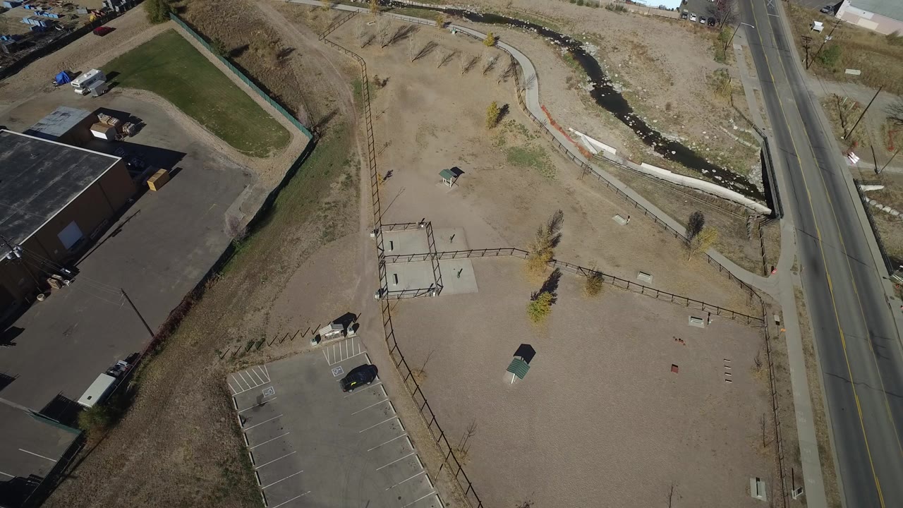 Aerial view of fenced open lot beside a road and industrial building.