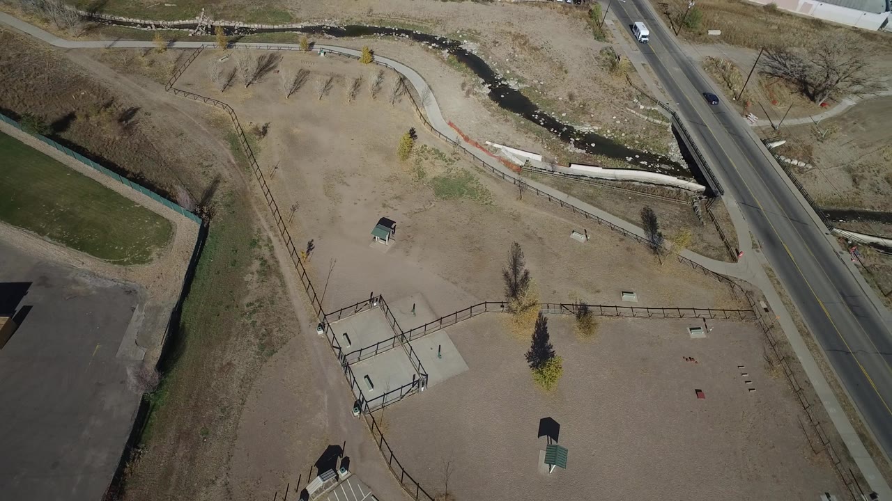 Westminster, Colorado aerial view with the road and bridge more central, creek winding across the top, tan park areas, a green grass patch, and small distant people.