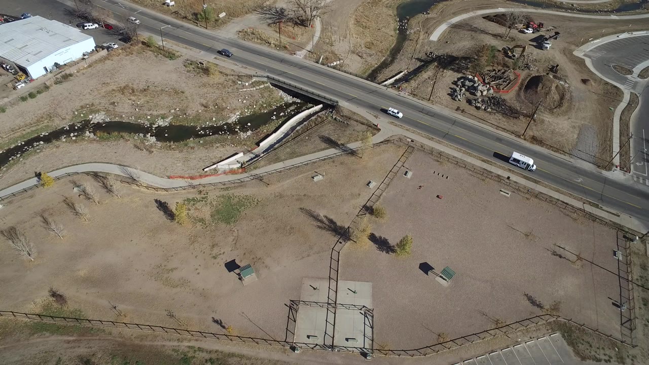Aerial view in Westminster, Colorado showing dry beige open land below a road bridge, a narrow drainage channel, curving paths, and no visible people.