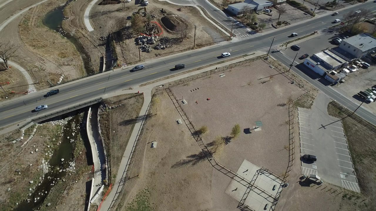 Overhead view of a road, parking lot, gravel area, creek channel, and cars.