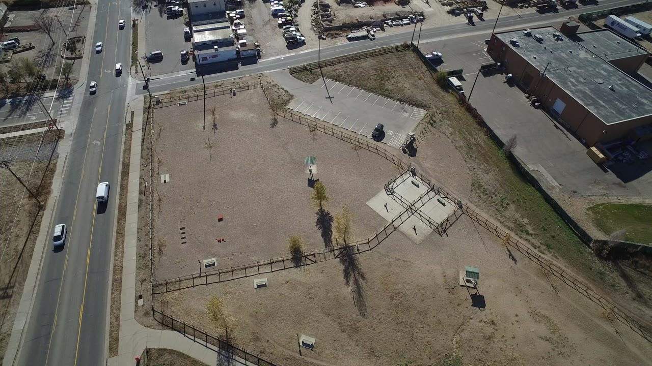 Aerial view of a fenced dirt playground beside a two-lane road and low buildings.
