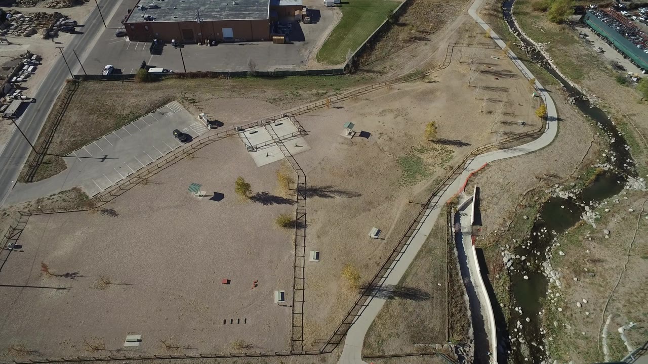 Drone view of a vacant parcel near a creek channel and parking area.