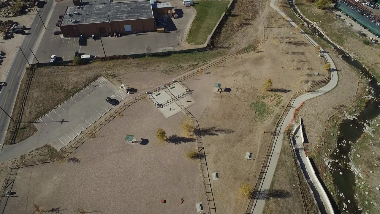 Overhead view of a dry park area beside a narrow creek and nearby buildings.
