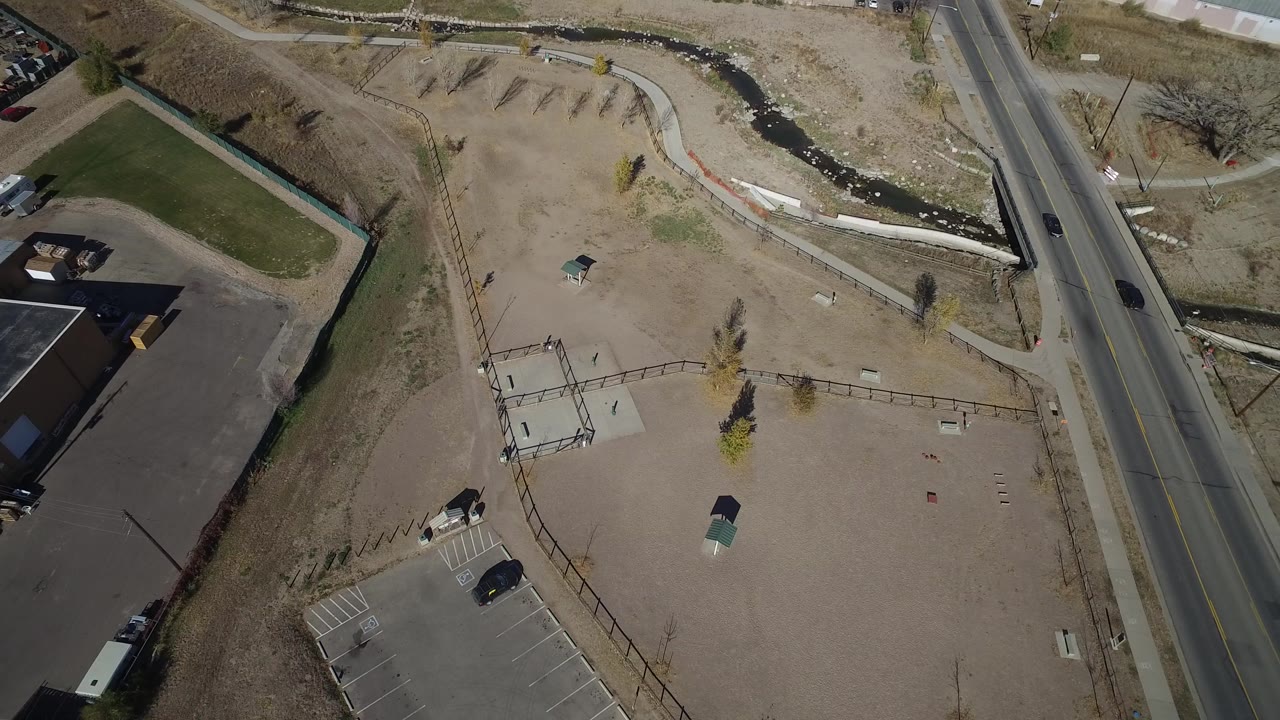 Overhead view of road, industrial building edge, parking lot, dirt lot, and drainage channel.