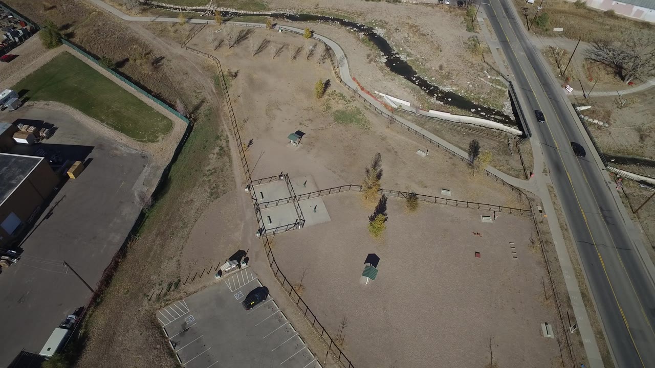 Aerial view in Westminster, Colorado with the road running vertically near the right side, open tan ground across the center, a dark-roofed warehouse at lower left, and no visible people.