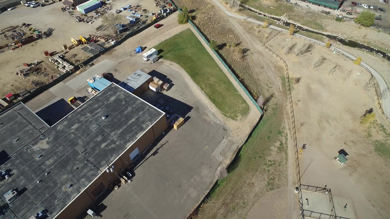 Aerial view of a flat-roof building beside a service road and dry grass corridor.