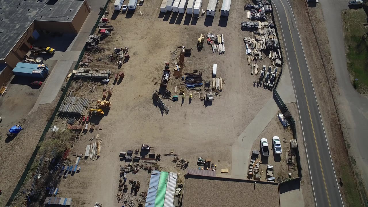 Overhead view of a gravel equipment yard beside a paved road.