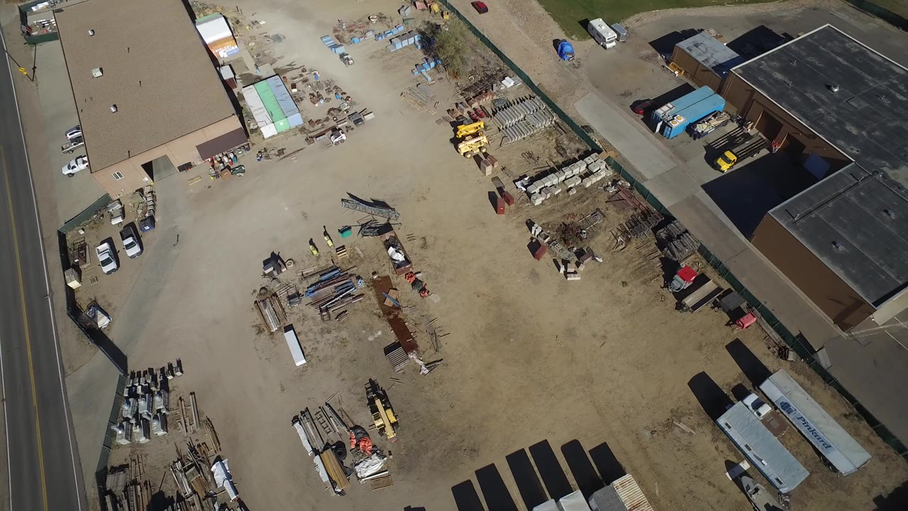 Overhead construction yard with roads, buildings, equipment, and stacked materials.
