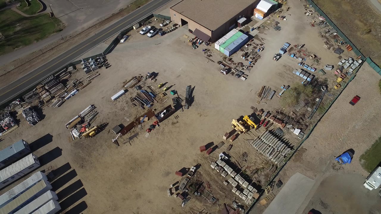 Overhead view of a dirt industrial lot with trailers, equipment, roads, and a large building edge.