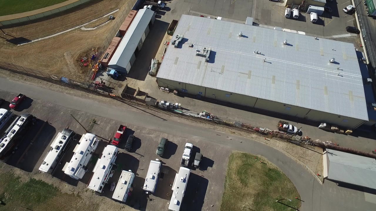 Overhead view of an industrial building with buses, trucks, cars, and a curved road.