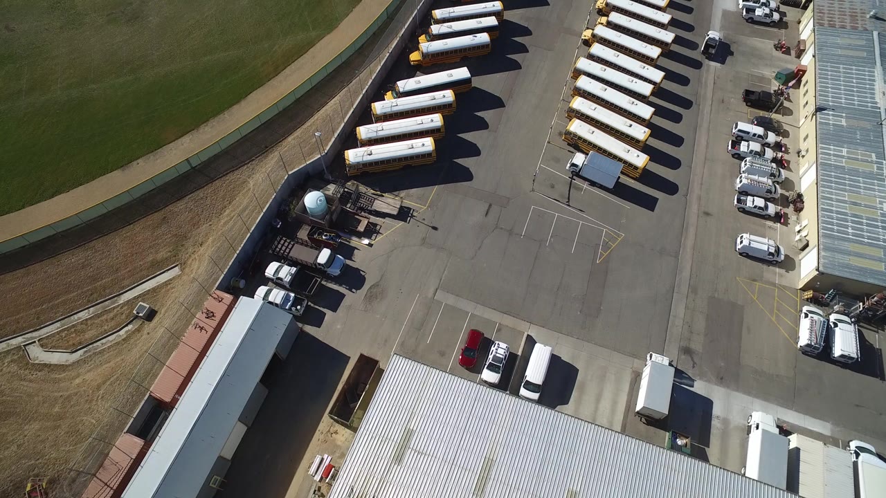Overhead Westminster, Colorado frame with two rows of buses, cars along a building, service vehicles, and the curved field boundary at left, with no visible people.