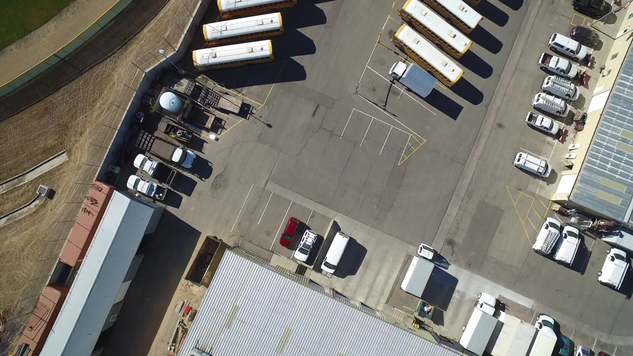 Overhead view of an industrial yard with trailers, parked vehicles, and a metal roof.