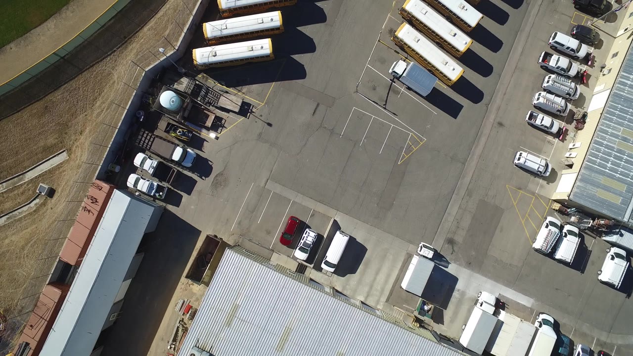 Aerial frame in Westminster, Colorado with long white trailers along the upper edge, service vehicles near a shed, a red car in the lot, and no clearly visible people.