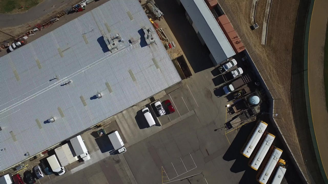 Overhead view of a large metal-roofed industrial hangar and parking lot.