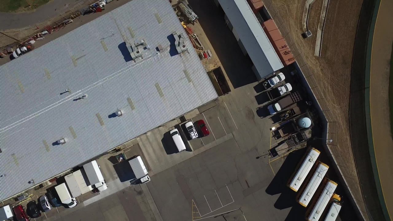Top-down Westminster, Colorado aerial with the corrugated hangar roof filling most of the frame, white box trucks and cars at the lower edge, and no visible people.