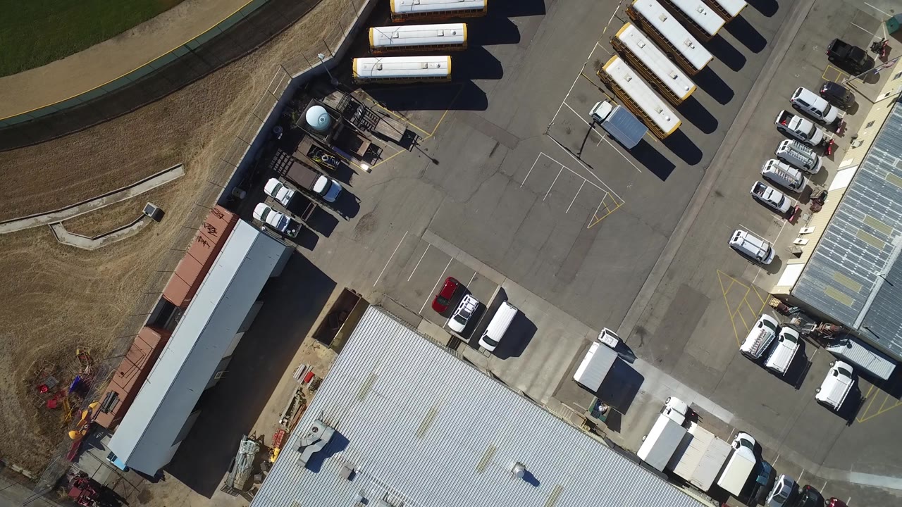 Top-down Westminster, Colorado frame with the vehicle yard shifted slightly in view, showing rows of white buses or trailers at the top, a long shed at left, parked cars near the center, and no visible people.