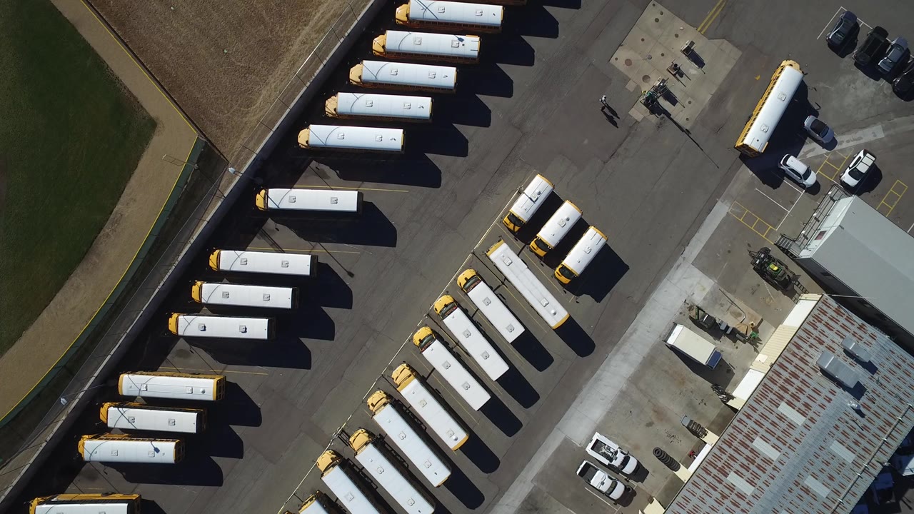 Overhead view of white and yellow transport vehicles in an industrial parking lot.