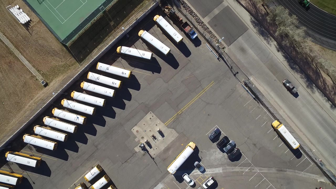 Aerial view of school buses parked beside tennis courts and a road.