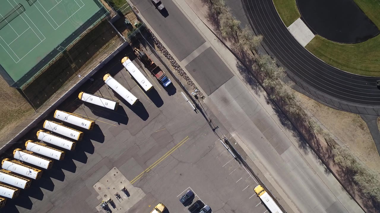 Overhead view of tennis courts, road, track, and parked school buses.
