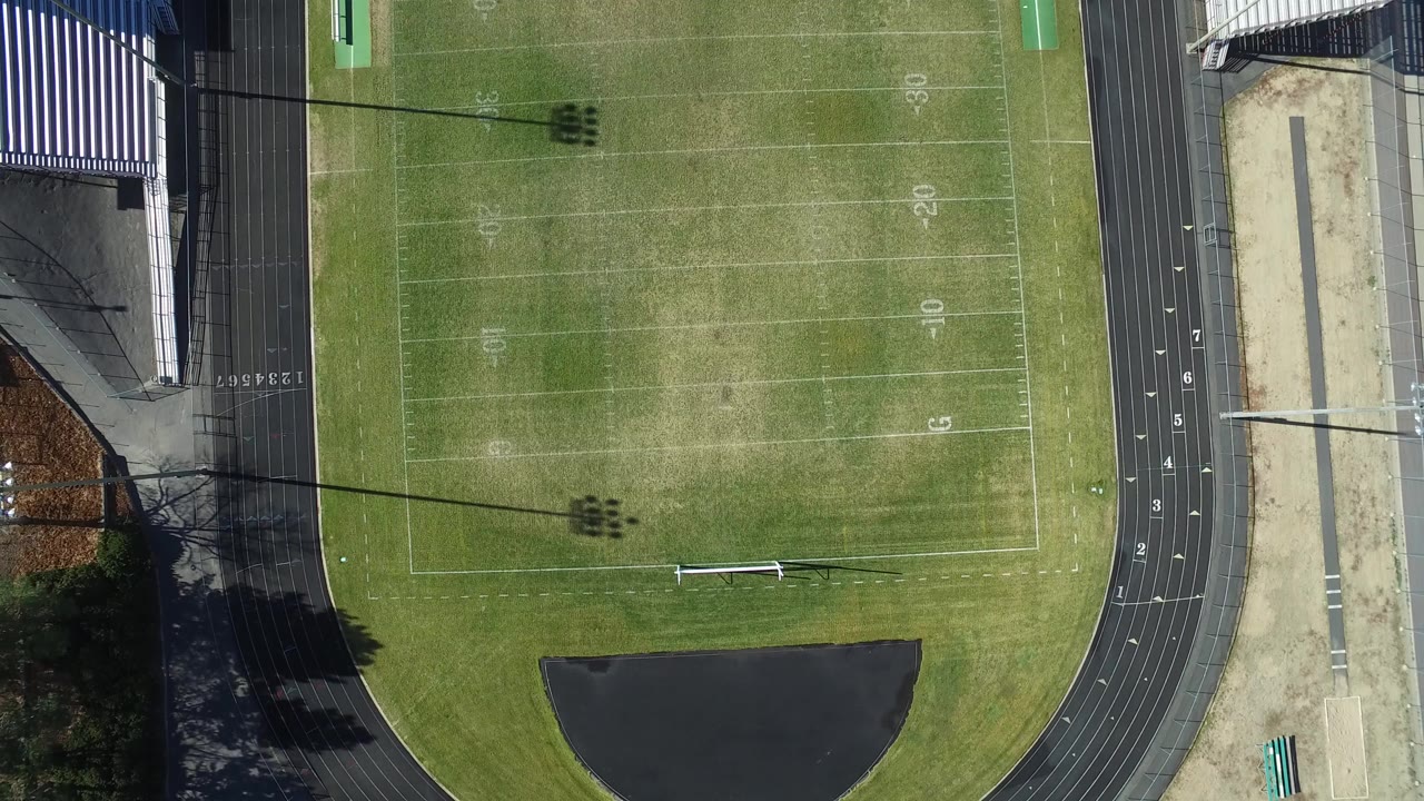 Overhead view of a green sports field beside a gray running track.