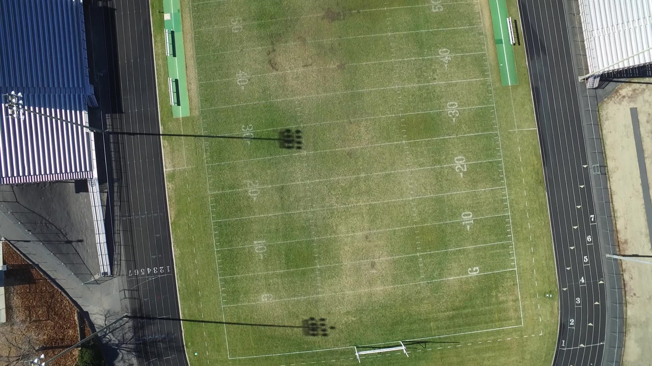 Top-down stadium view with field markings, bleachers, and a track.