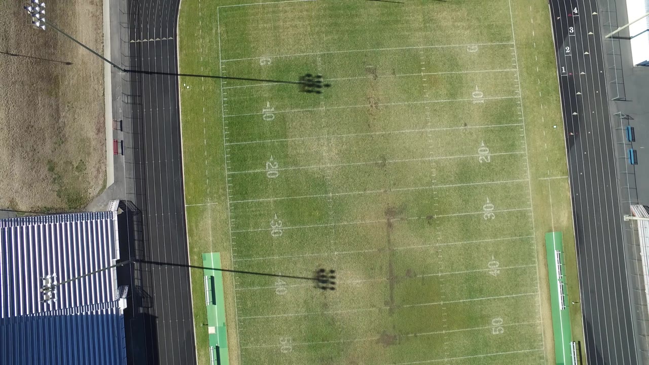 Aerial view of football field with track lanes and light shadows.