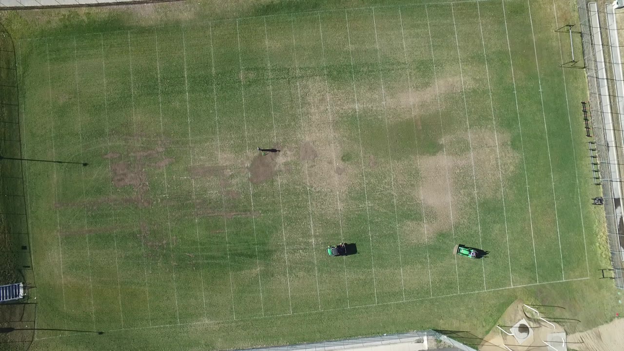 Overhead Westminster, Colorado field view with pale yard markings, patchy grass areas, two small green maintenance objects on the turf, and no visible people.