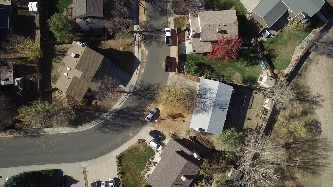 Overhead frame of a Westminster, Colorado residential block with rooftops, driveways, lawns, parked cars, tree shadows, and no visible people.