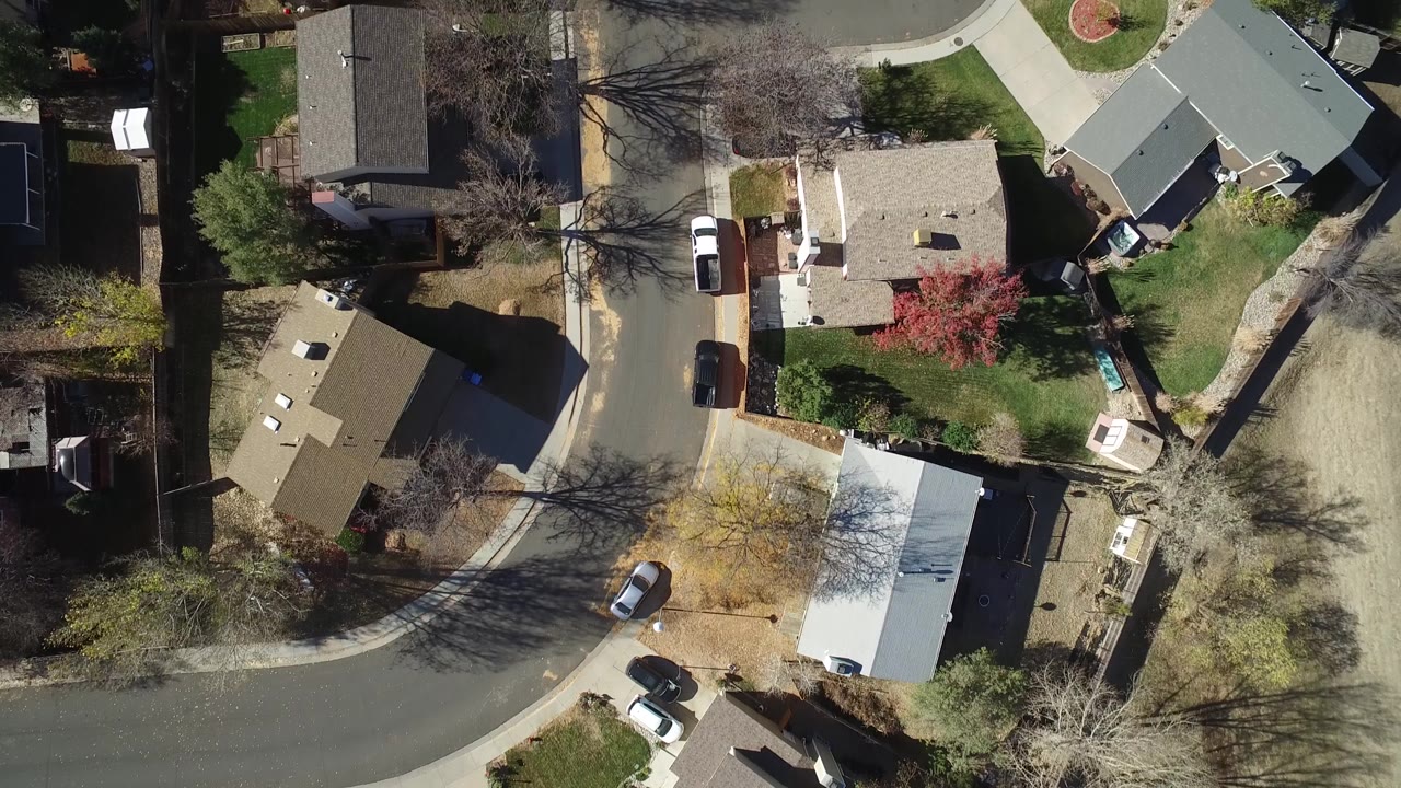 Top-down neighborhood view with houses, lawns, and a small red tree.