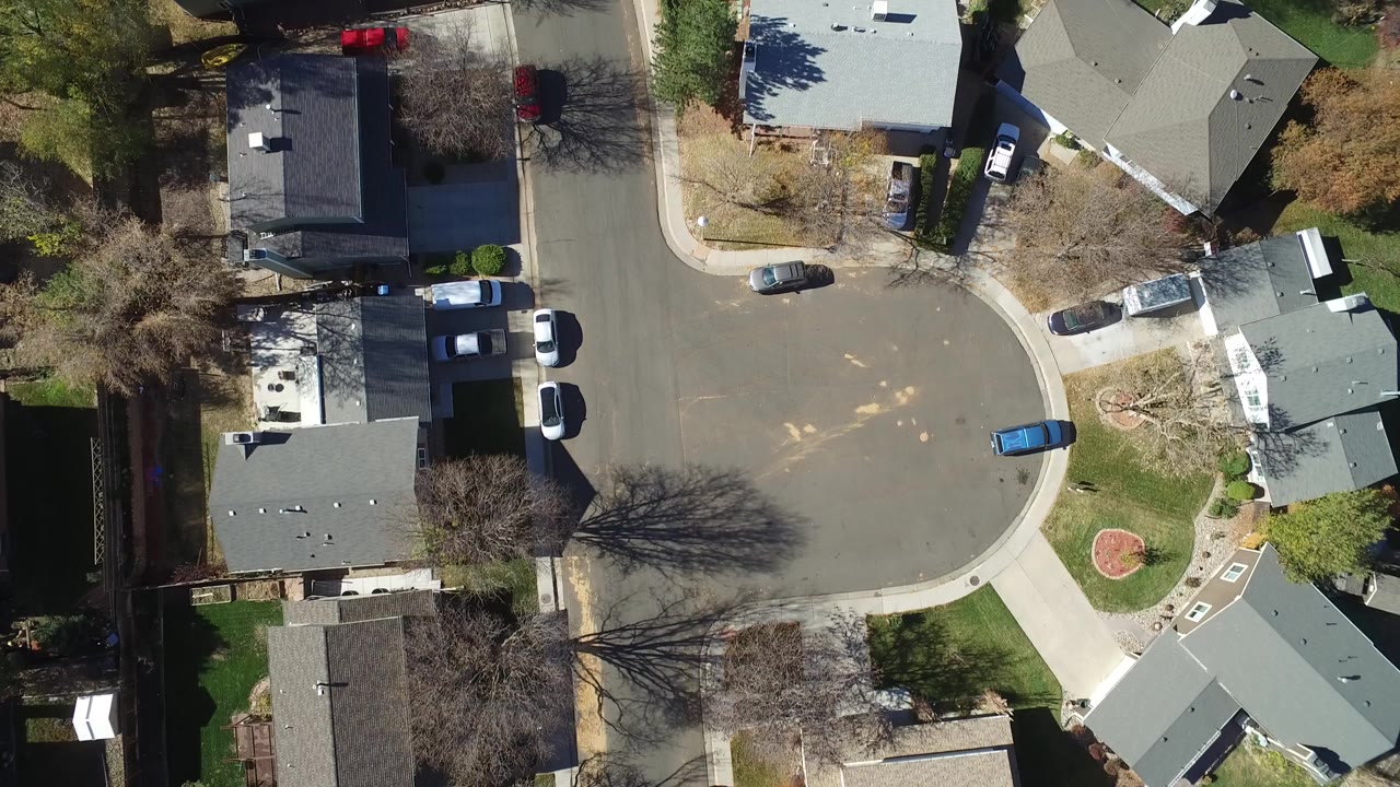 Overhead view of a suburban cul-de-sac with houses, parked cars, lawns, and trees.