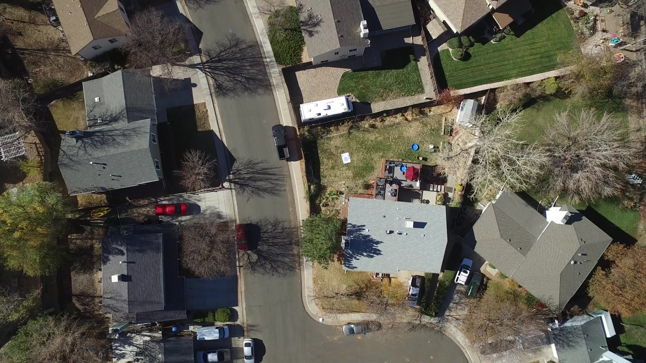 Overhead view of suburban houses, a curved street, parked cars, and leafless trees.
