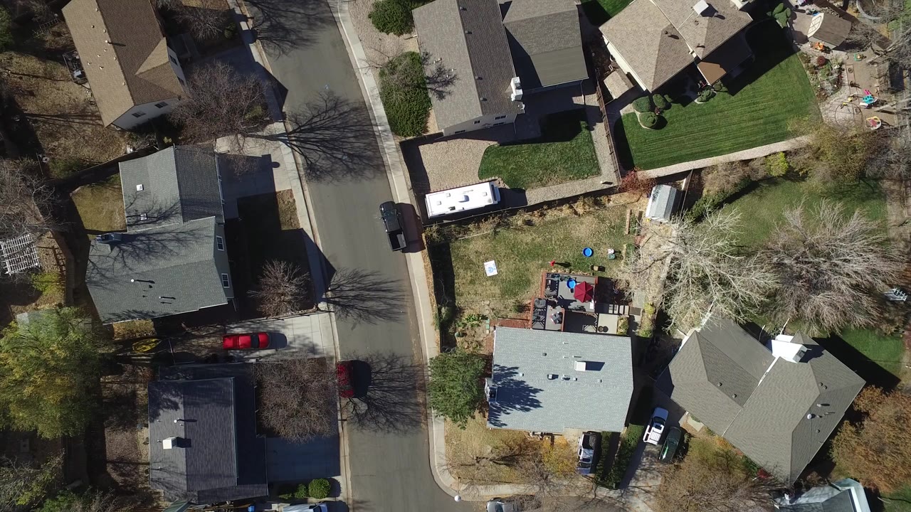 Top-down drone view of a Westminster, Colorado residential block with detached homes, driveways, parked cars, yards, leafless trees, and no visible people.