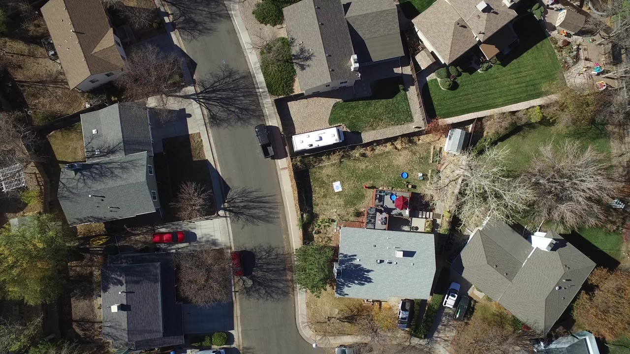 Top-down neighborhood view with houses, a street, lawns, trees, and vehicles.