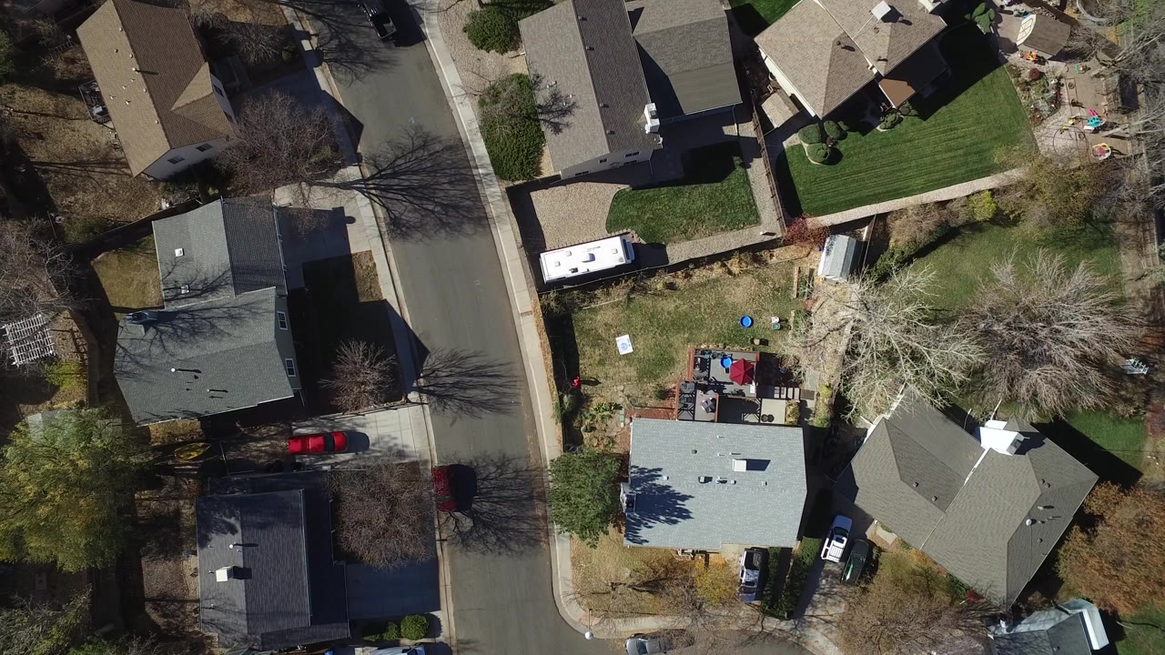 Top-down aerial view of suburban houses, backyards, trees, and a curved street.