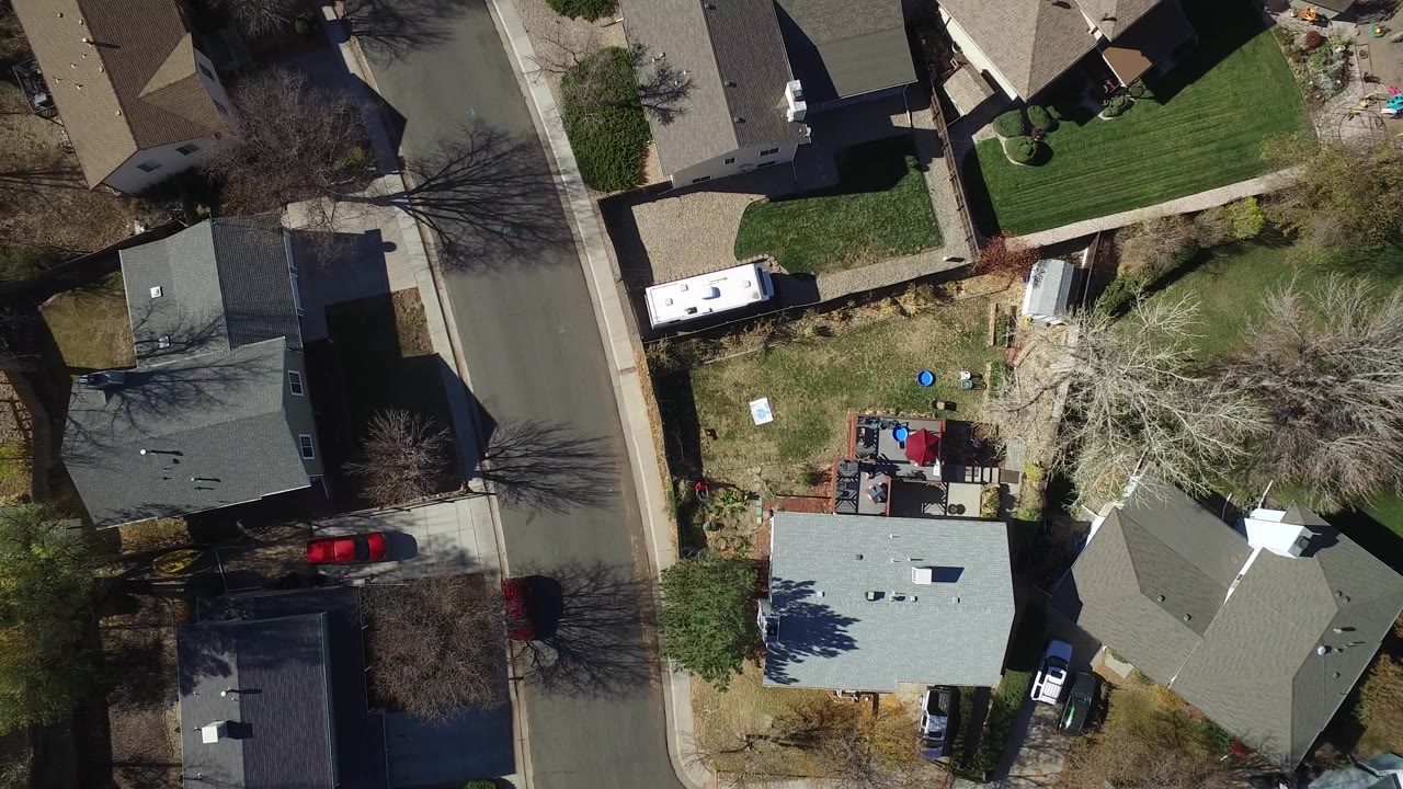 Opening overhead frame of a Westminster, Colorado residential block with gray-roofed homes, a curved street, lawns, leafless trees, parked cars, and no visible people.