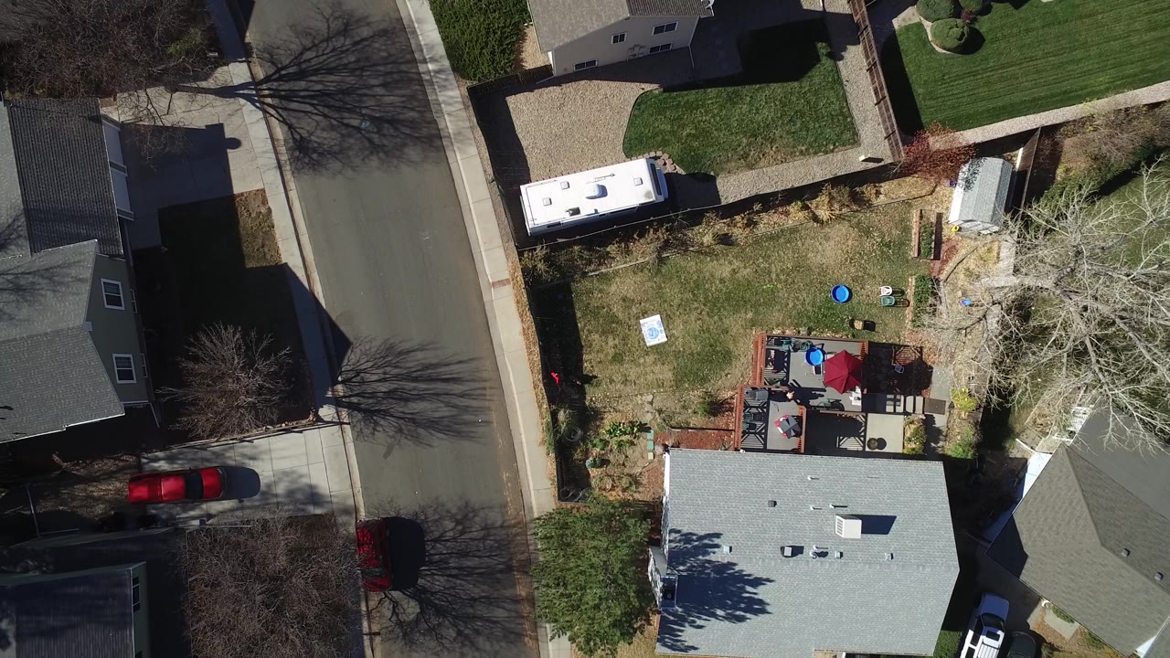 Overhead view of a suburban house, yard, street, and parked caravan.