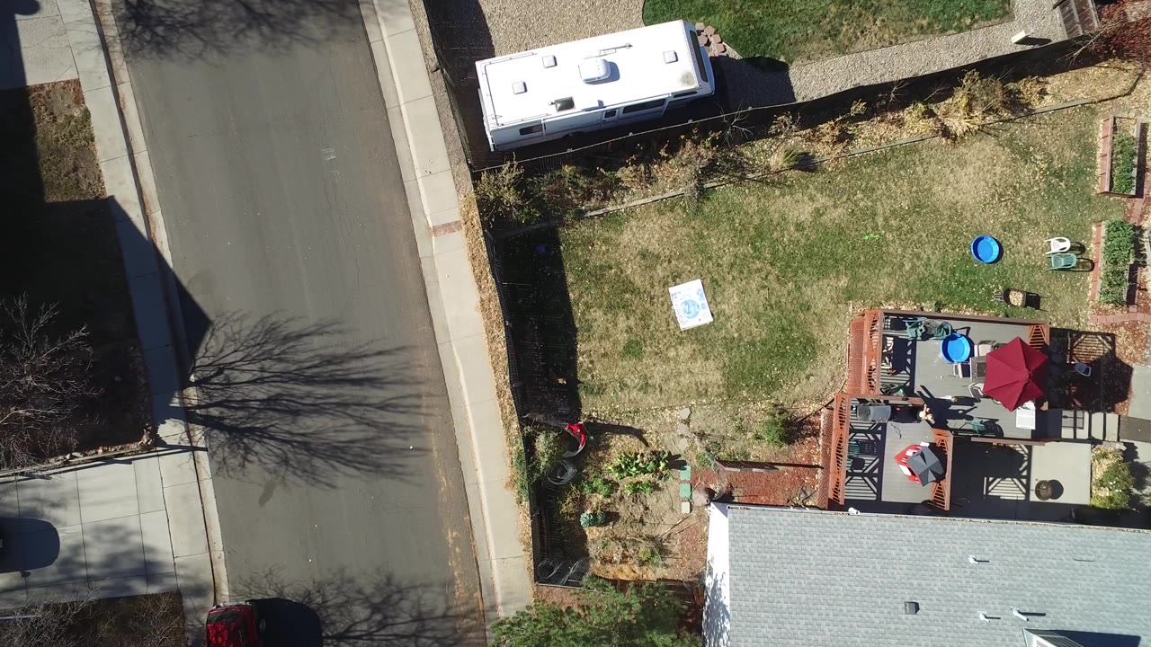Top-down Westminster, Colorado frame showing the residential road and sidewalk on the left, the RV along the upper edge, the lawn and small patio objects in the middle, and tiny people on the deck.