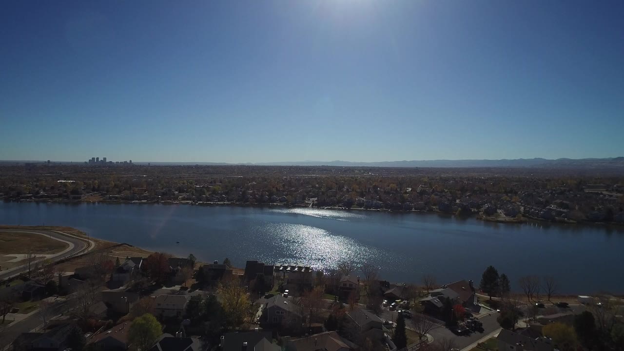 Aerial view over homes toward a sunlit lake and distant skyline.