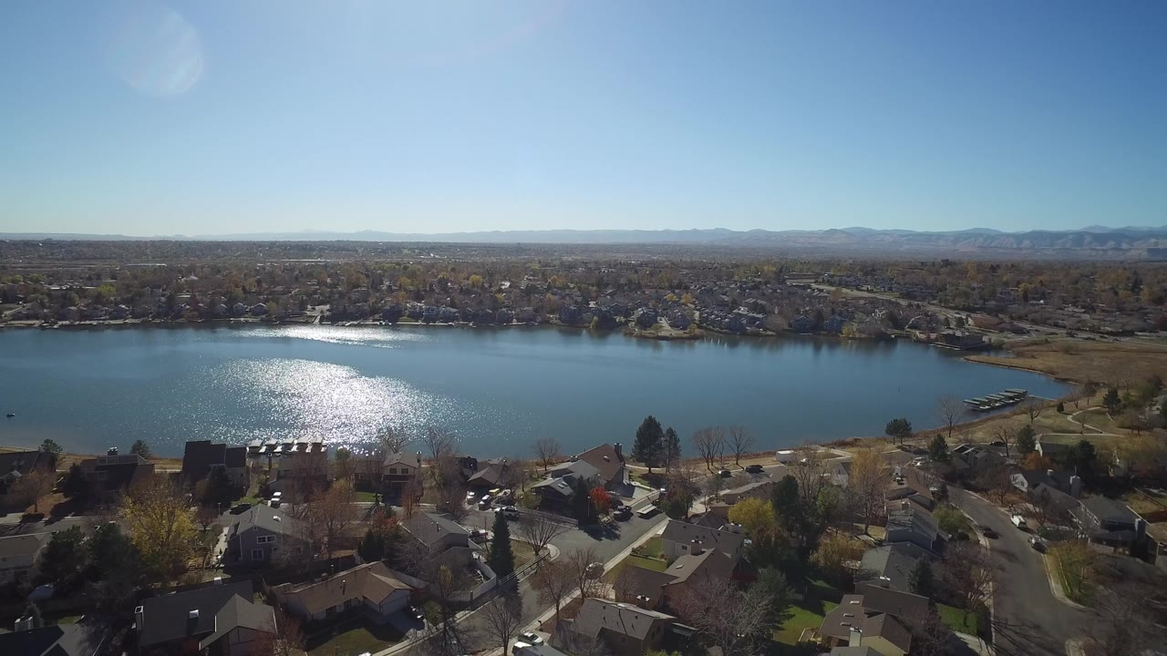 Aerial view over homes toward a blue lake and distant horizon.