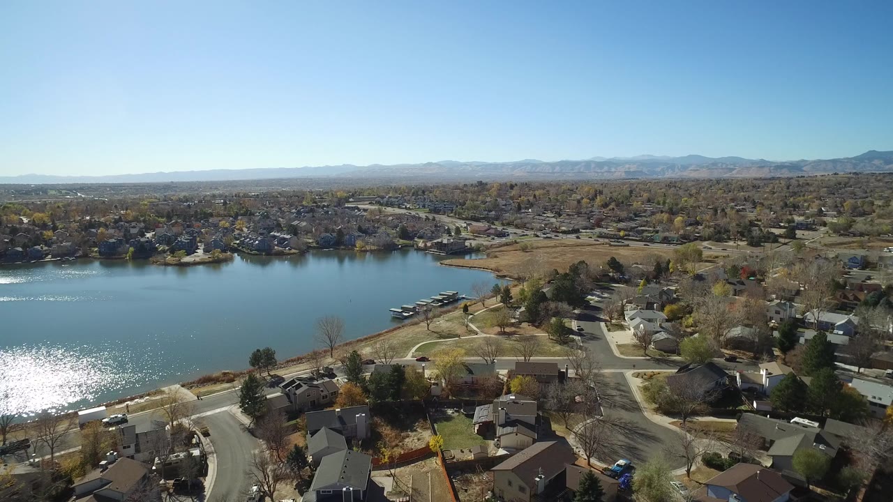 Aerial view of a lake beside residential streets and homes under a clear blue sky.