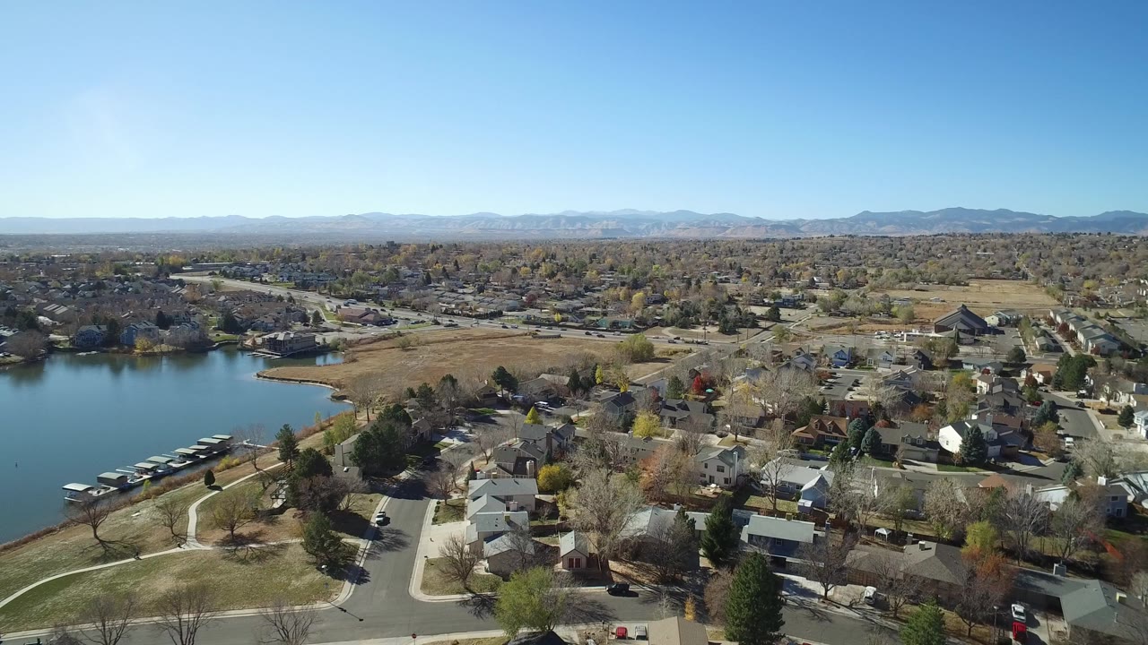 High aerial view of houses, streets, trees, a lake, and distant mountains.