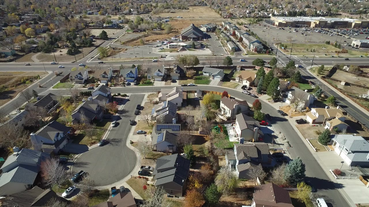 Aerial frame over Hidden Lake, Colorado houses, a curved cul-de-sac, parked cars, a larger road beyond the homes, and no visible people.