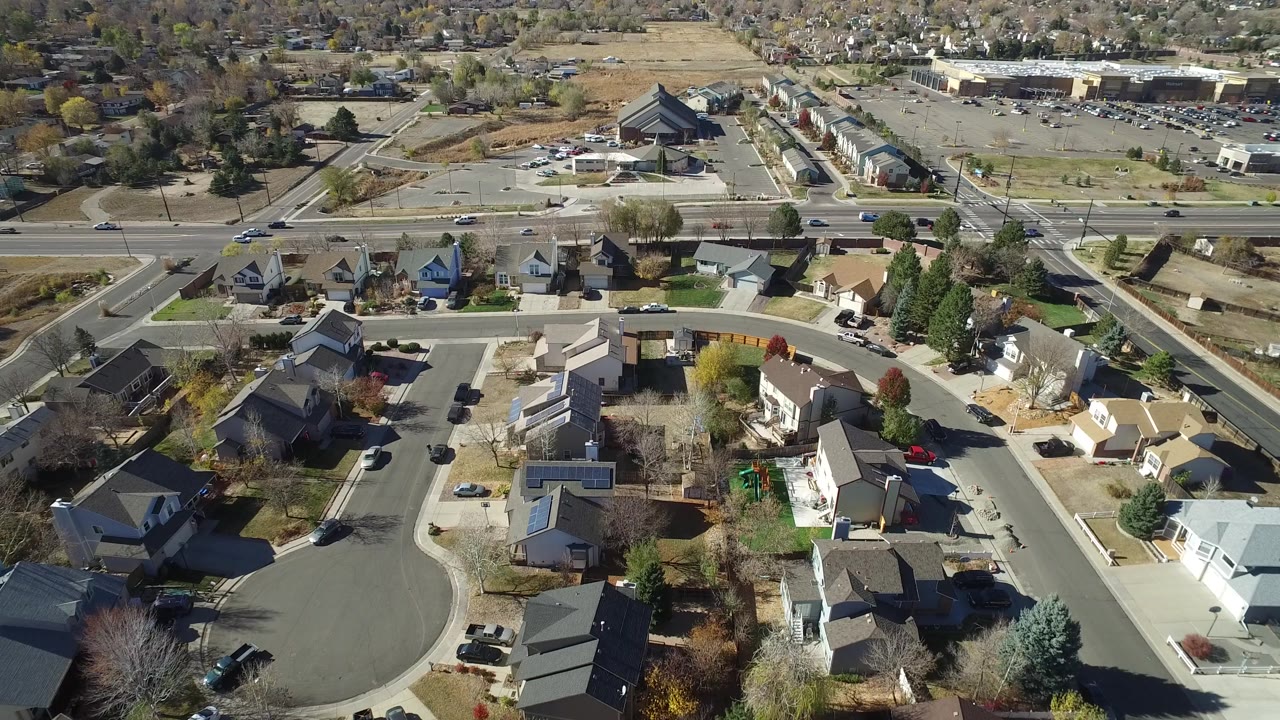 Aerial neighborhood view with houses, a cul-de-sac, dry yards, and open land beyond a road.