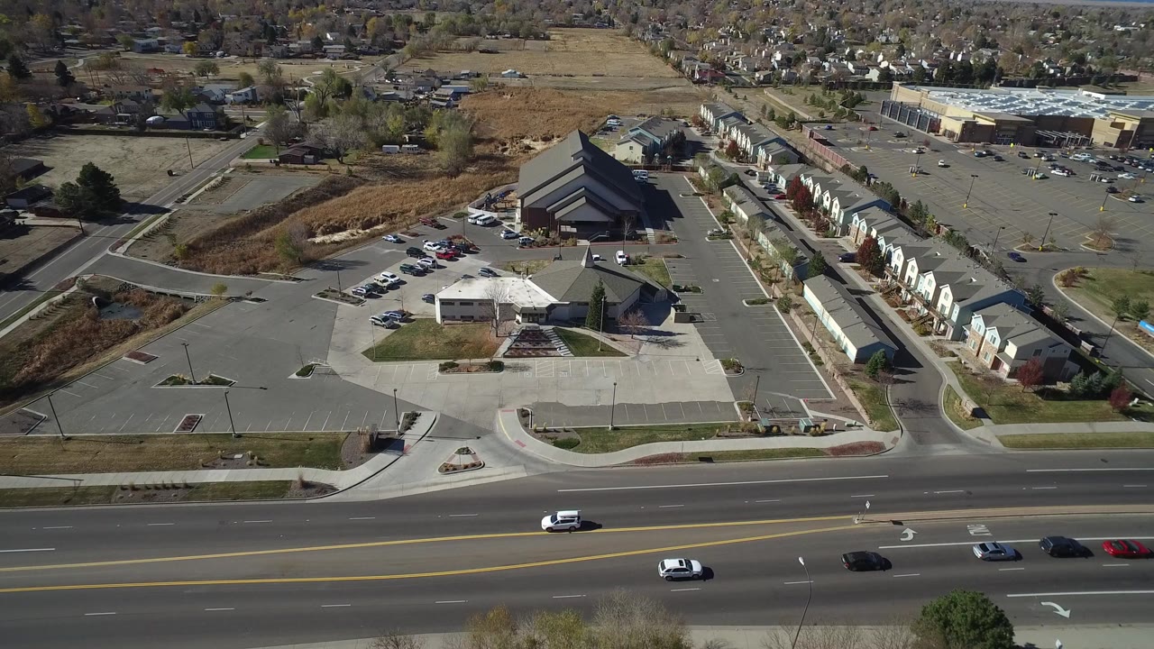 Hidden Lake, Colorado aerial frame with cars on the foreground road, a large paved lot, a dark angular-roof building, attached homes to the right, and no visible people.