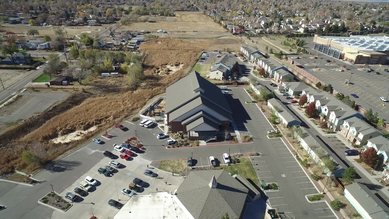 Aerial view in Hidden Lake, Colorado, with the parking rows and dark-roofed building more centered, bordered by small buildings, roads, and distant homes.