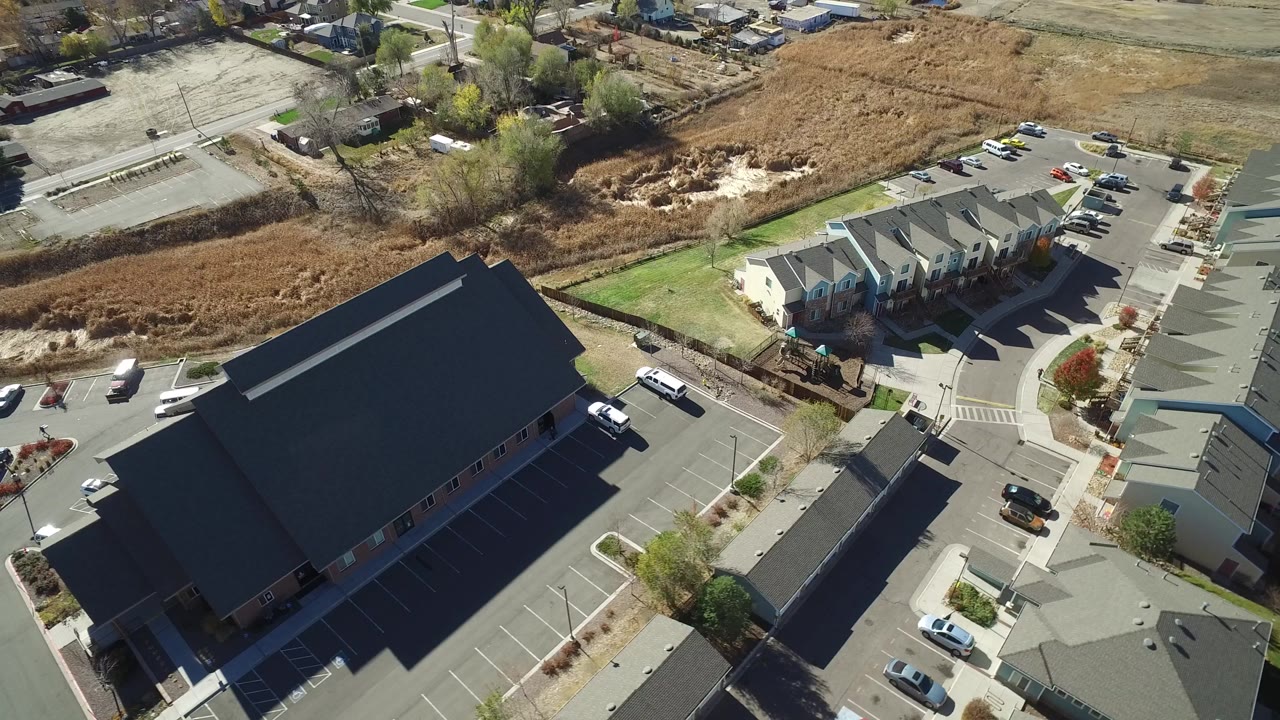 Aerial view of a dark-roofed building beside townhouses and parking lots.