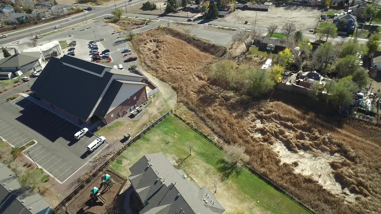 Aerial view of a parking lot and large building bordering a tan reed field and residential yards.