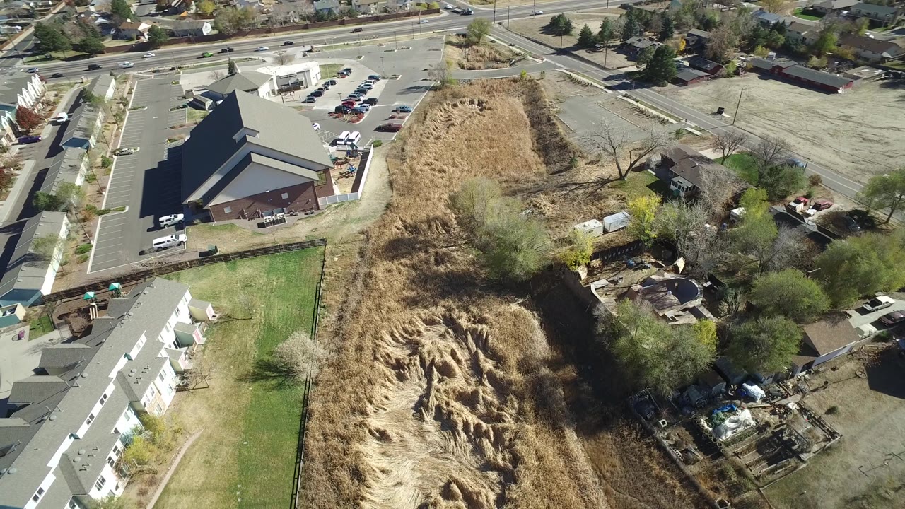 Drone view of a suburban block with townhomes, parking areas, roads, and open lots.