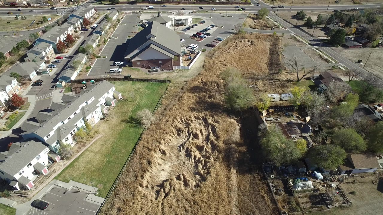 Aerial view of townhomes, open grassland, roads, and parked cars.